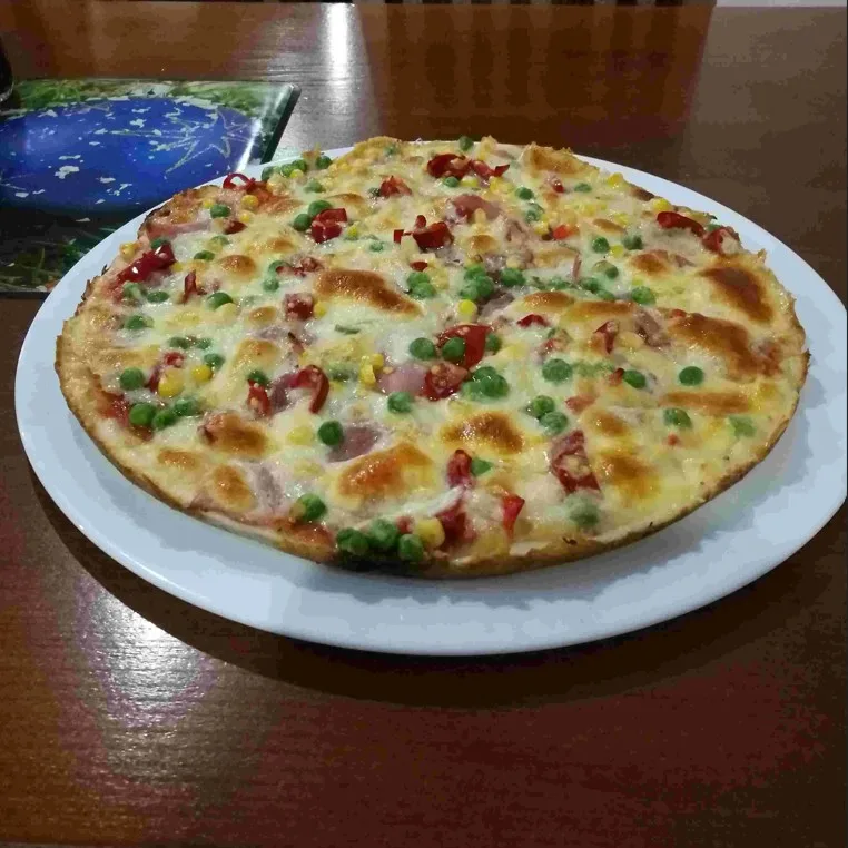 Detailní pohled na pizzu se šunkou a zeleninou.